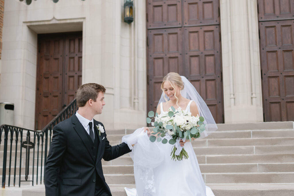 groom helping bride walk down steps outside of St Florian Catholic Church, located in Detroit Michigan