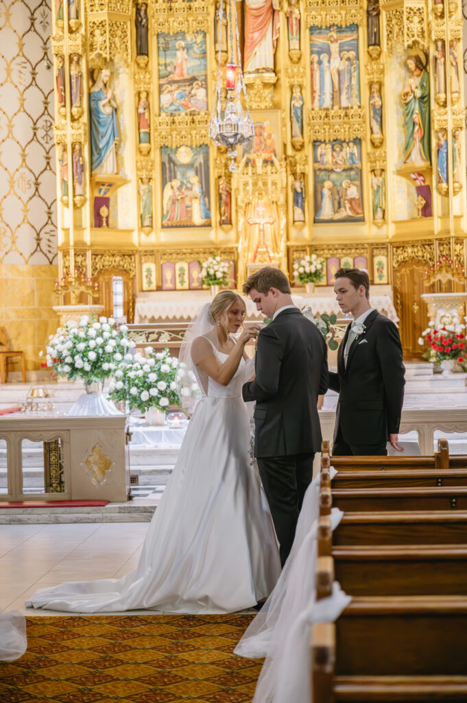 bride fixing groom's boutonniere inside St Florian Catholic Church, located in Hamtramck Michigan