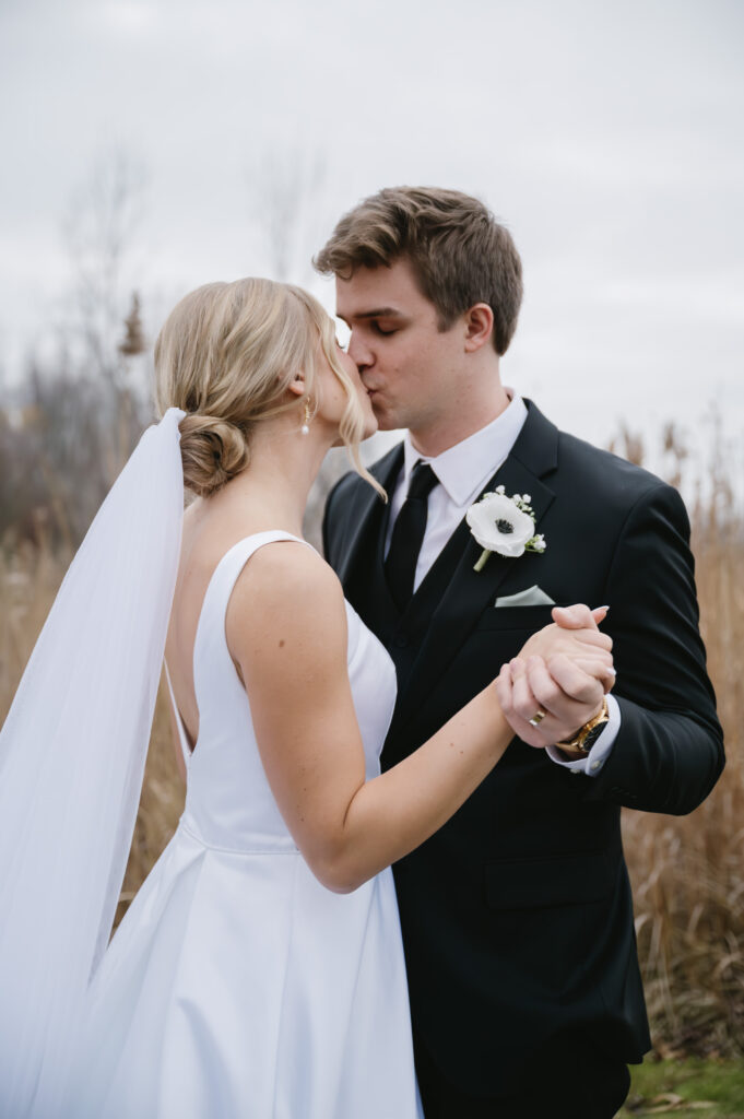 bride and groom kissing in open field near The Palazzo Grande, a Sterling Heights Michigan wedding venue