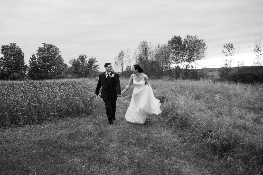 bride and groom running through field at barn wedding venue