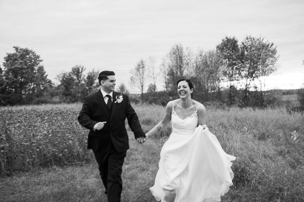 bride and groom running through field at Crooked River Weddings, a venue in Northern Michigan