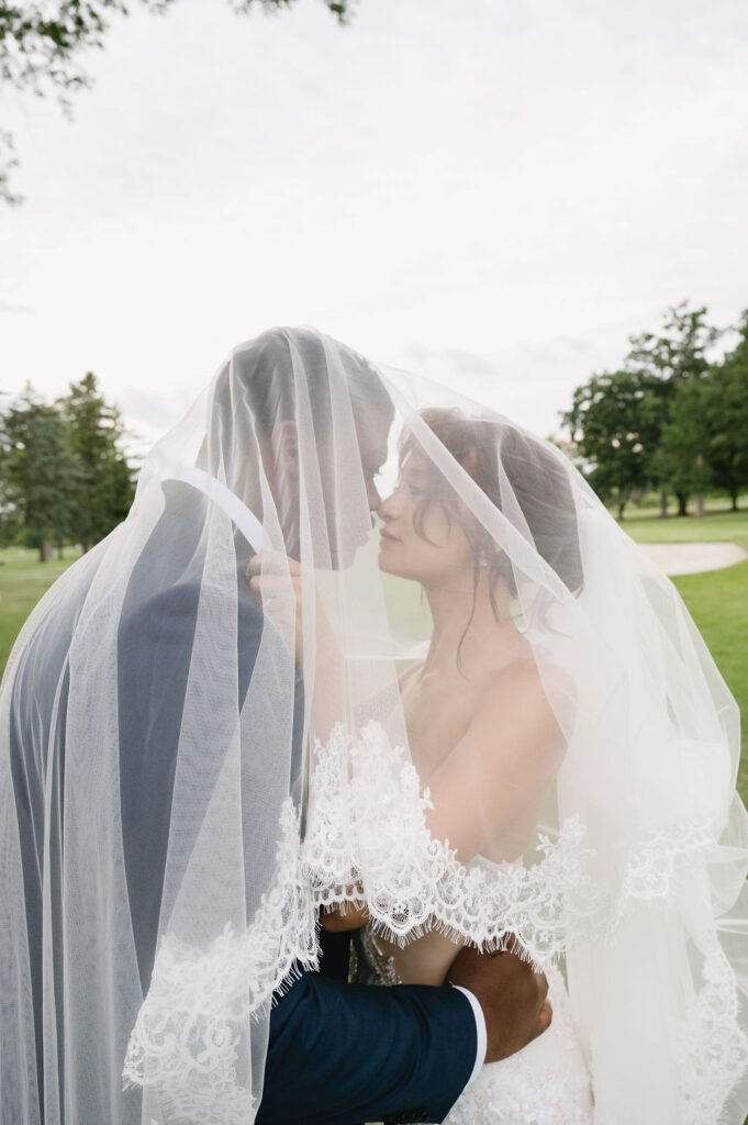 bride and groom under wedding veil on golf course