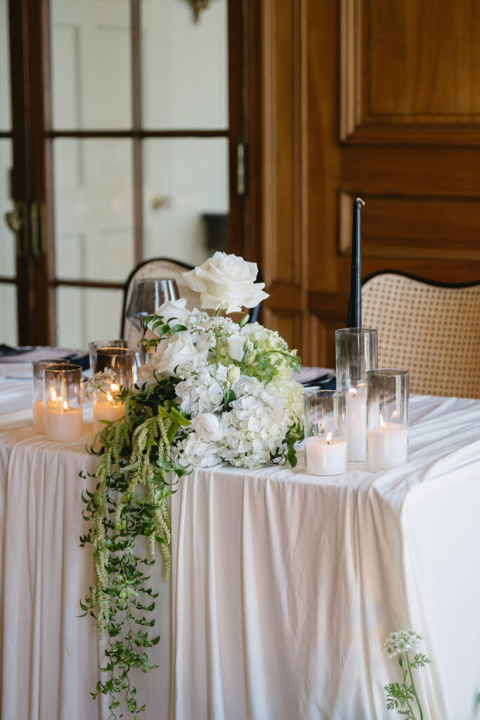 lit white candles on a sweetheart table with white florals and cascading greenery