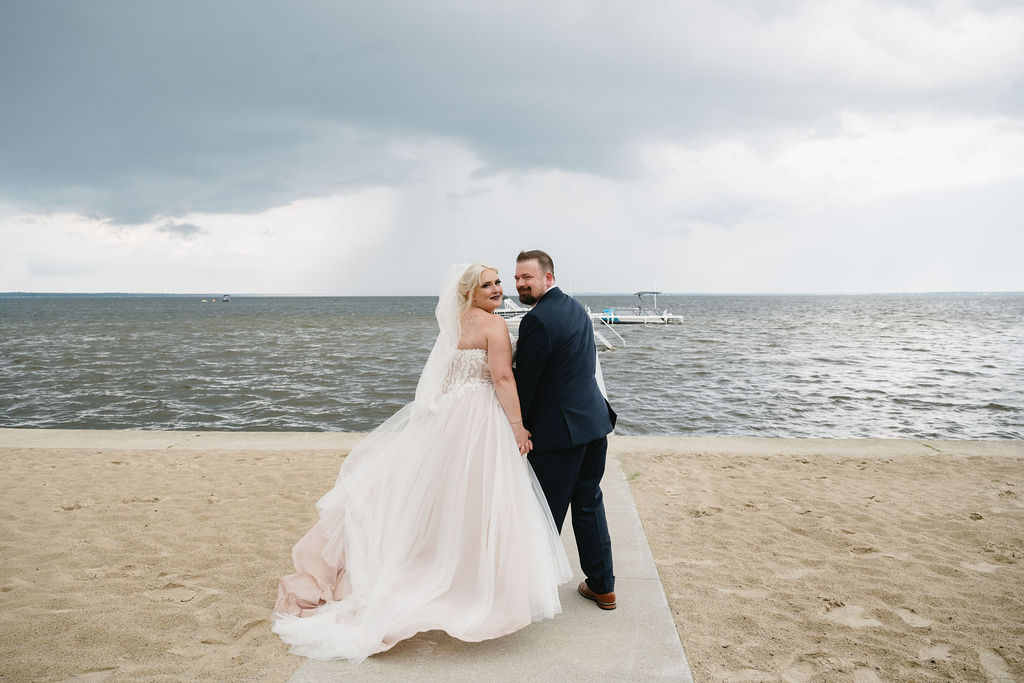 bride and groom standing on lakeside beach