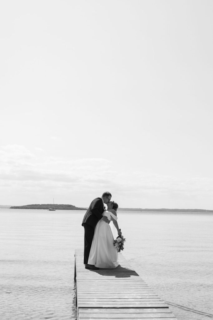 bride and groom kissing on lake dock