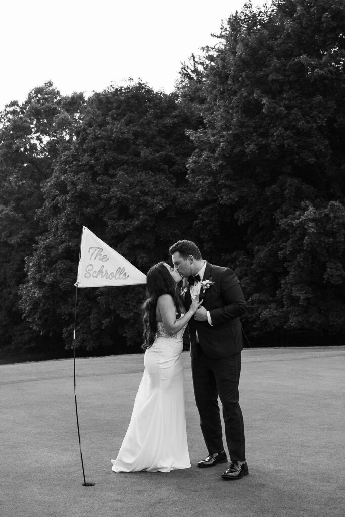 bride and groom kissing on golf course with personalized flag