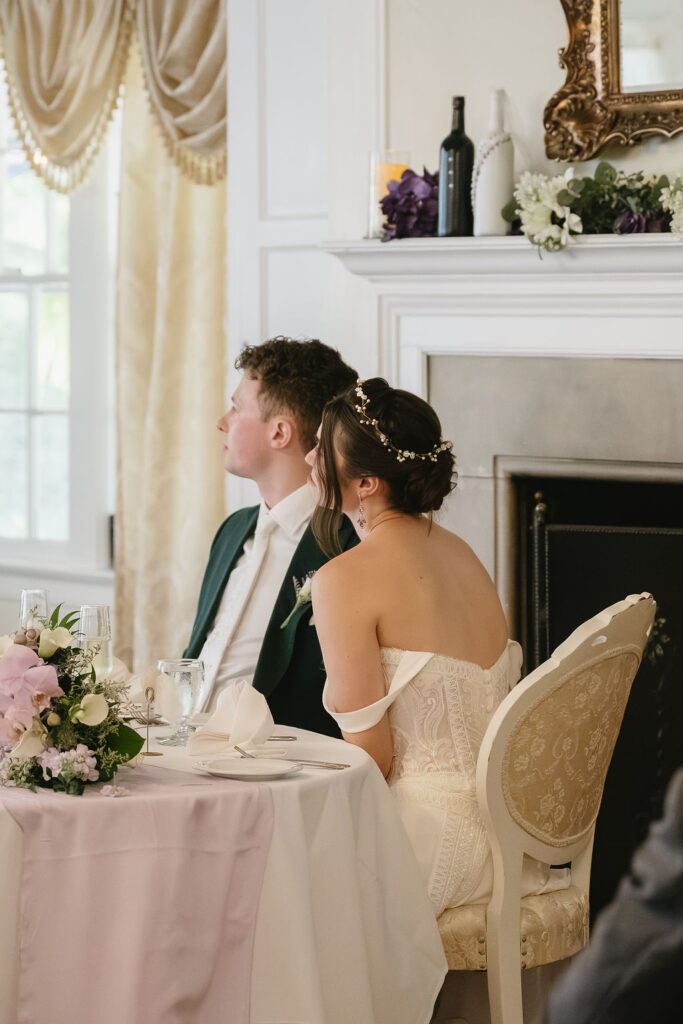 bride and groom sitting at table listening to wedding toast