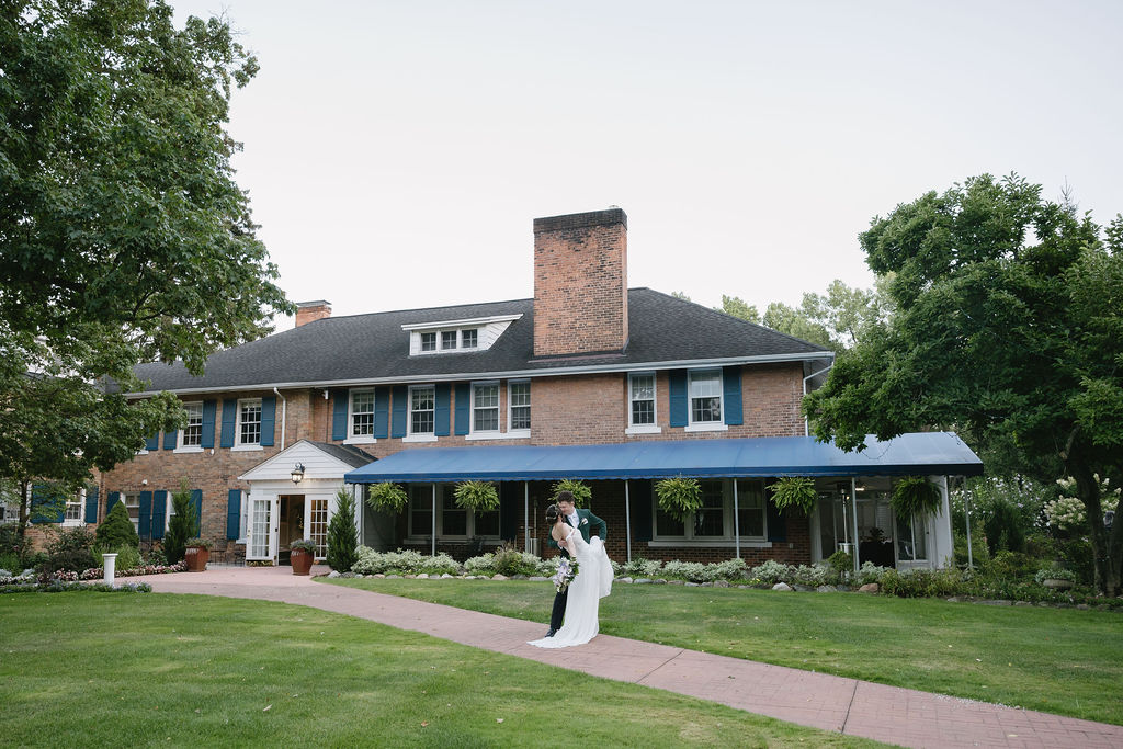 bride and groom kissing in front of longacre house wedding venue in farmington hills