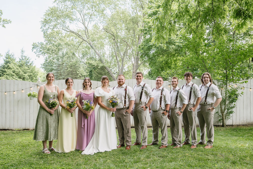 wedding party standing in front of white fence