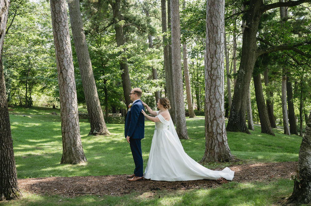 bride walking up behind groom for first look outside under trees