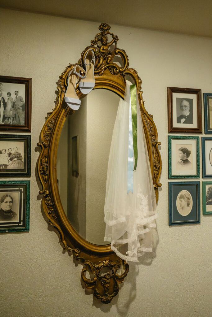 ornate gold mirror with blue heels and wedding veil hanging from top
